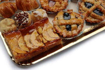 Traditional assortment of italian pastries on golden tray. Cannoli, Babà, cream puffs, small pies with jam, mini tart with cream and fruits and apple pie