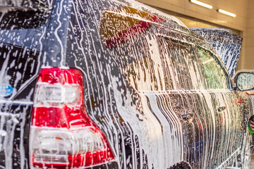 black SUV car washing at car wash station with soap foam