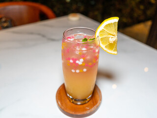 A piece of freshly cut yellow lemon slice placed on a cold glass.