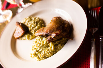 Dish duck leg with green perlotto served on a white plate