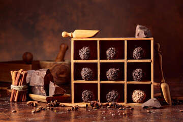 Chocolate candy in wooden box, broken pieces of chocolate, cinnamon sticks, anise and coffee beans.