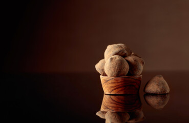 Chocolate truffles in small wooden dish sprinkled with cocoa powder. Black reflective background.