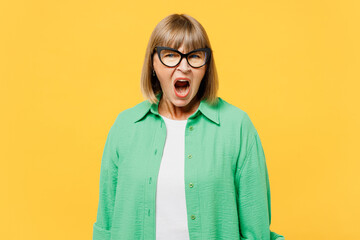 Elderly sad outraged furious angry blonde woman 50s years old wear green shirt glasses casual clothes look camera scream shout isolated on plain yellow background studio portrait. Lifestyle concept. - obrazy, fototapety, plakaty