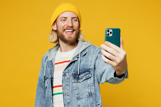 Young blond man he wears denim shirt hoody beanie hat casual clothes doing selfie shot on mobile cell phone post photo on social network isolated on plain yellow background studio. Lifestyle concept.