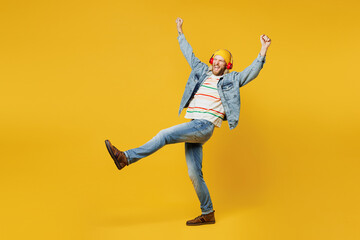 Full body young happy man he wear denim shirt hoody beanie hat casual clothes listen to music in headphones with raised up hands isolated on plain yellow background studio portrait. Lifestyle concept - obrazy, fototapety, plakaty