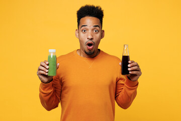 Young shocked sad man wear casual clothes hold show juice green vegetable smoothie, bottle of soda...
