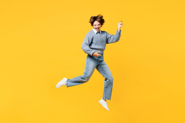 Full body expressive singer virtuoso young woman she wearing grey knitted sweater shirt casual clothes jump high play air guitar isolated on plain yellow background studio portrait. Lifestyle concept.