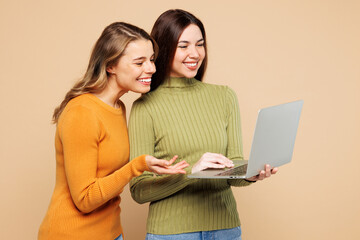Side view young friends two IT women they wear orange green shirt casual clothes together hold use...