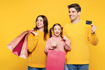 Young parent mom dad child kid girl 7-8 years old wear pink casual clothes hold shopping package bags credit bank card look aside isolated on plain yellow background Black Friday sale buy day concept