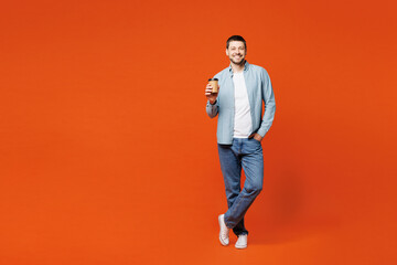 Full body young man wears blue shirt white t-shirt casual clothes hold takeaway delivery craft paper brown cup coffee to go isolated on plain red orange background studio portrait. Lifestyle concept.