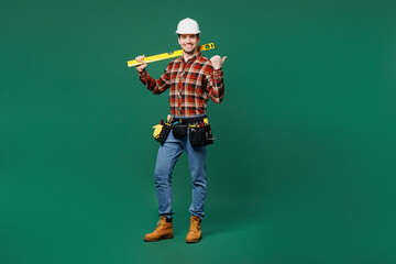 Full body young employee laborer man he wears red shirt hardhat hat work hold level tool point aside isolated on plain green background. Instruments for renovation apartment room Repair home concept.