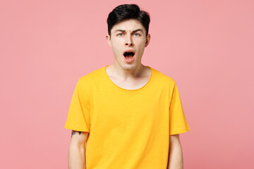 Young sad dissatisfied displeased Caucasian man wears yellow t-shirt casual clothes look camera with opened mouth scream shout isolated on plain pastel light pink background studio. Lifestyle concept.