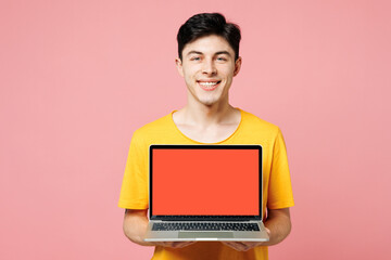 Young IT man wears yellow t-shirt casual clothes hold use work on laptop pc computer with blank screen workspace area isolated on plain pastel light pink background studio portrait. Lifestyle concept.