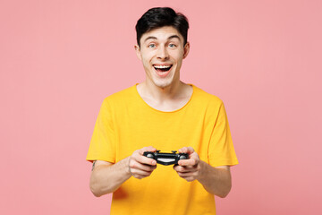 Young surprised excited man he wearing yellow t-shirt casual clothes hold in hand play pc game with joystick console isolated on plain pastel light pink background studio portrait. Lifestyle concept.