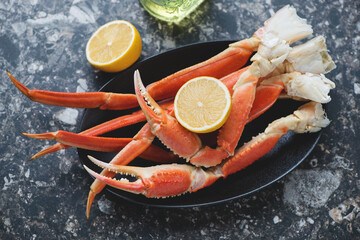 Black plate with boiled opilio or snow crab and lemon, horizontal shot on a dark-brown granite...