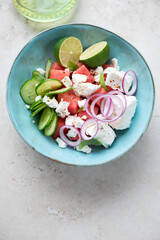 Turquoise bowl with watermelon, cucumber and feta cheese salad, vertical shot on a light-beige stone background with space, top view