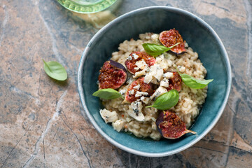 Bowl of risotto with fig fruits, blue cheese and fresh basil, horizontal shot on a brown granite...