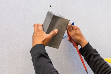 An electrician installs a rectangular accent light fixture on the outside wall.