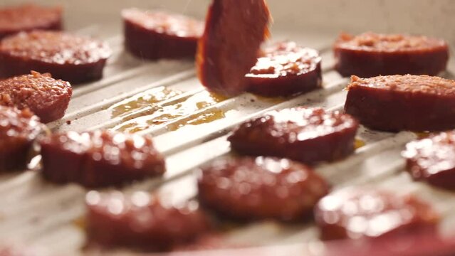 Cooking Turkish Sausage Also Known as Sucuk in Pan. Unrecognizable Person Flipping Sliced Meats to Roast Perfectly. Preparing for Breakfast Close Up Shot Slow Motion. Camera Moving Left to the Right. 