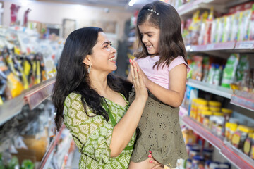 Happy indian mother and daughter enjoying at grocery store. Mother holding her daughter hands in supermarket.