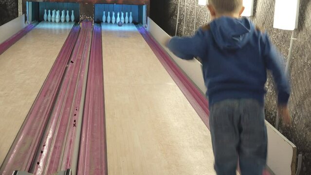 Little kid hits the ten pins with bowling ball and jumping of joy for winning the game