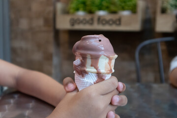 A young child's hand holding a dripping chocolate ice cream cone in the cafe