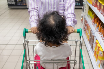 A mother pushing a shopping cart dan her child sitting in trolley in supermarket