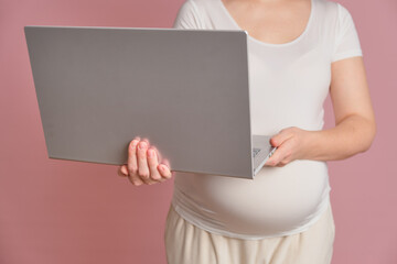Pregnant woman holding a laptop in her hands, studio pink background. Pregnancy and modern technology concept