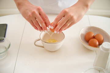 Close-up of female hands cracking egg into bowl on kitchen table. Process of cooking pecan pie in...