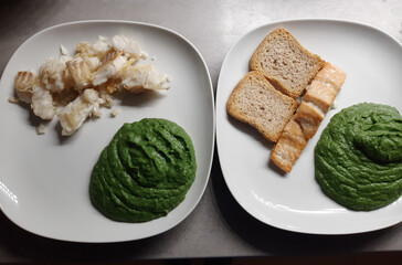 Homemade baked trout and salmon with spinach sauce pure and sliced bred served on two white plates