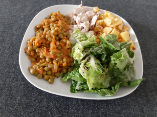 Homemade grilled chicken with french fries, green salad and pea stew served on a white plate