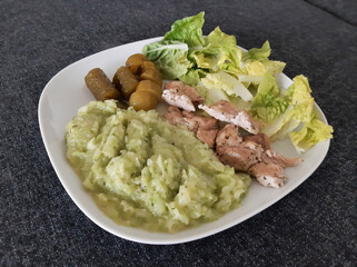 Homemade grilled chicken with zucchini stew, green salad and cucumber pickles served on a white plate