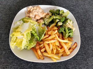 Homemade grilled chicken with french fries, broccoli and green salad, served on a white plate