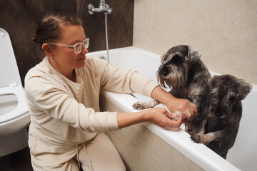 Beautiful young woman taking care of her dog in the bathroom. Pet care concept.