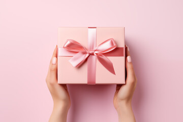 Top view of a female hands holding a pink gift box on pale pink background with copy space