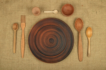 Rustic eating utensils, empty ceramic plate, traditional wooden spoon, fork and bowl, served on canvas tablecloth, close up, elevated table top view, directly above