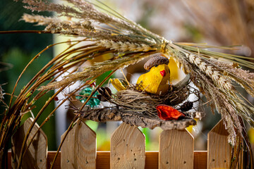 Sunny Spring Composition: Handcrafted Bird's Nest with Yellow Bird Figurine on Bright Wooden Fence Amidst Colorful Blurred Background