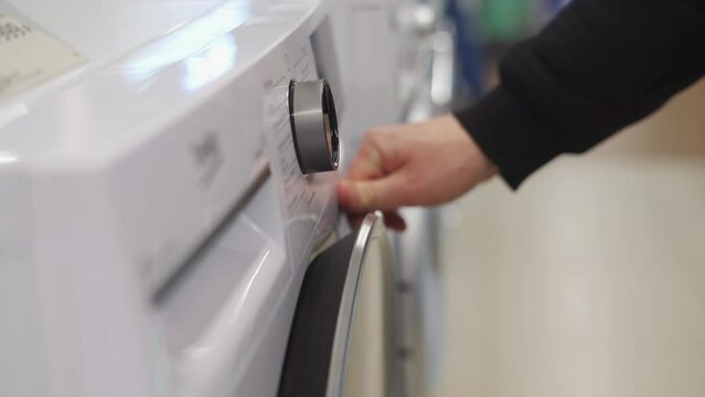 A white man's hand adjusts the knob on a washing machine
