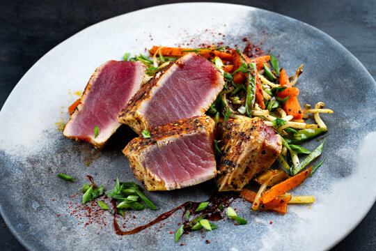 Traditional Japanese gourmet tuna fish steak tataki with vegetable slices and soy sprouts with sweet dour sauce served as close-up on a Nordic design plate with copy space