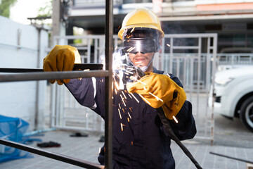 Asian worker wearing safety suit uses a welding machine. The sparking of the welding wire and steel...