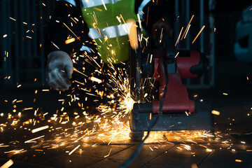 Close up Asian worker wearing a safety suit uses a steel cutting (circular saw) industry machine to cut steel creating a trail of sparks.