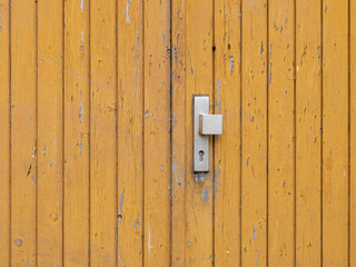 Old wooden door with an old filthy knob. The entrance is weathered and aged. The exterior paint is peeling off and dirt stains are on the facade. Close up of an old fashioned building wall.