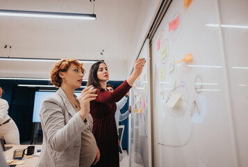 Creative business professionals collaborate in a dynamic workshop, sharing ideas and discussing statistics on a whiteboard for successful project planning and profitability.