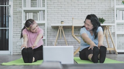 Asian mother and daughter stretch their legs on yoga mat to warm up before practicing exercise with...
