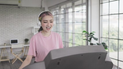 portrait of Young Asian woman enjoys listening to music and exercising on machine treadmill at home