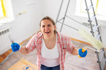 Frustrated woman with paintbrush and roller during home renovation