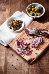 Sliced french salami with fresh rosemary and olives on rustic wooden background.	