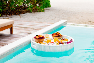 served floating tray in swimming pool with drinks and snacks on tropical island resort in Maldives,...