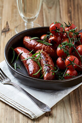 Grilled sausages with cherry tomatoes and fresh rosemary. Rustic wooden background