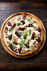 Pizza with mozzarella cheese, marinated tomatoes and fresh rocket. Dark wooden background. Top view.	